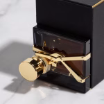 A close-up, studio-lit photograph of a premium product package, such as a dark-colored perfume bottle with gold accents and textured paper box, placed on a marble surface with soft shadows, symbolizing luxury and high perceived value.